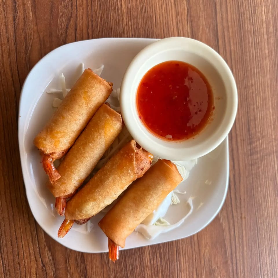 Four crispy shrimp spring rolls served on a white plate with red dipping sauce.