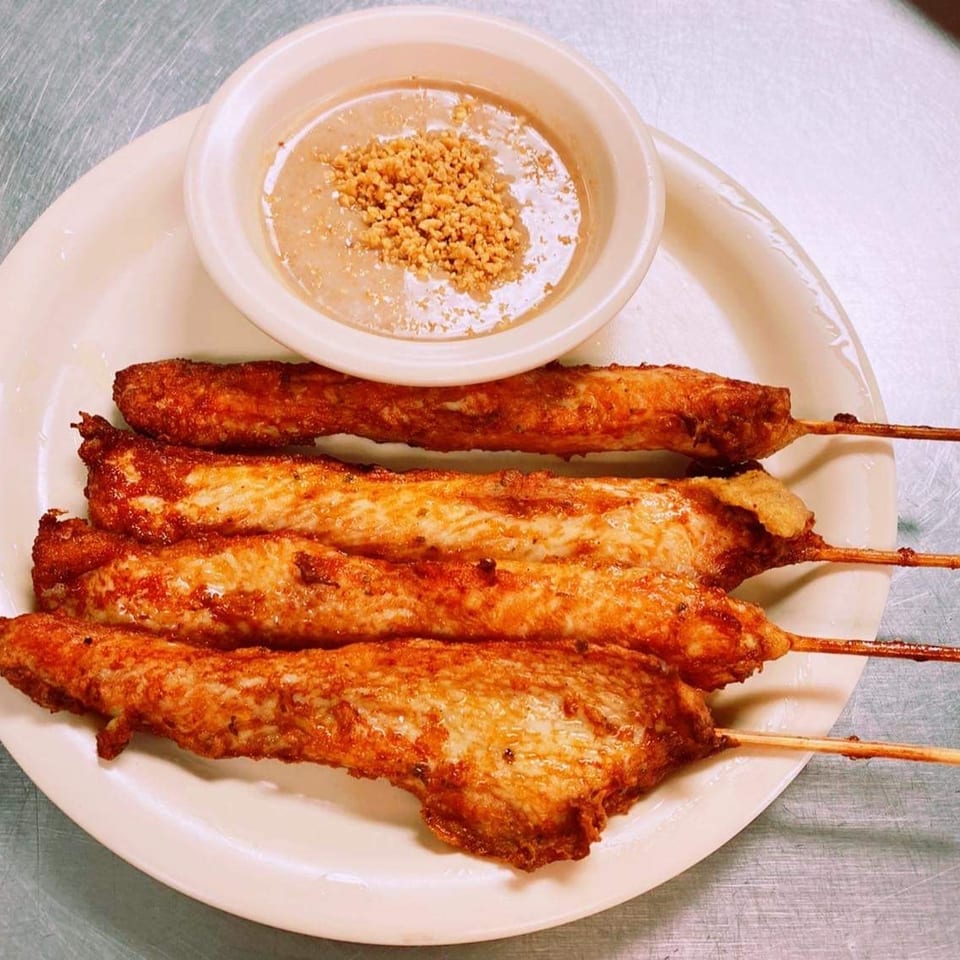 Grilled meat skewers arranged on a plate with a small bowl of dipping sauce topped with crushed peanuts.