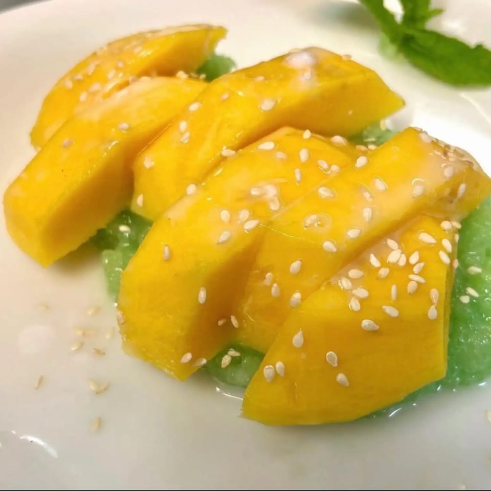 Golden sesame-topped dumplings arranged on leafy greens and served on a white plate.