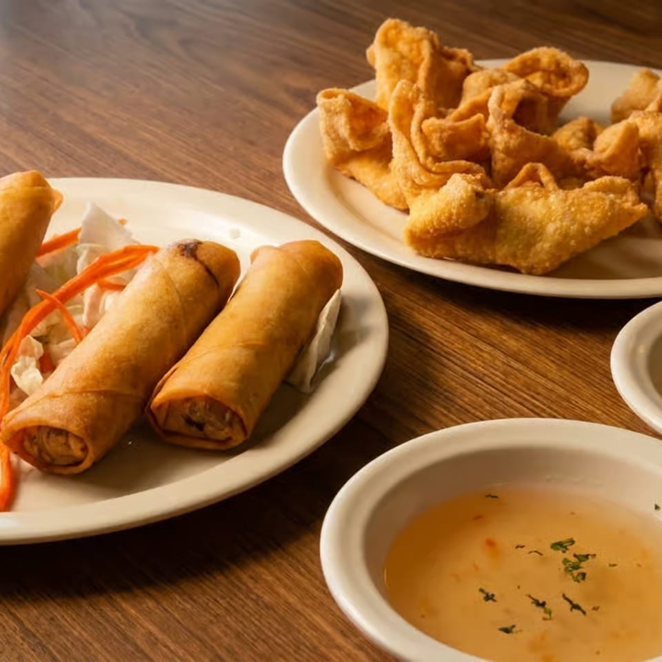Golden spring rolls and crispy dumplings served on plates with shredded vegetables and dipping sauces on a wooden table.