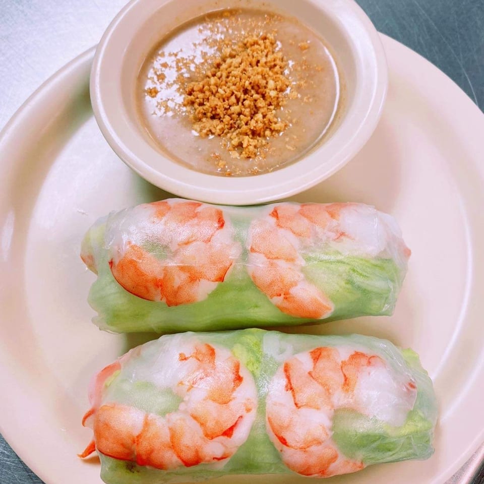Two shrimp spring rolls with lettuce served alongside a bowl of peanut dipping sauce on a plate.